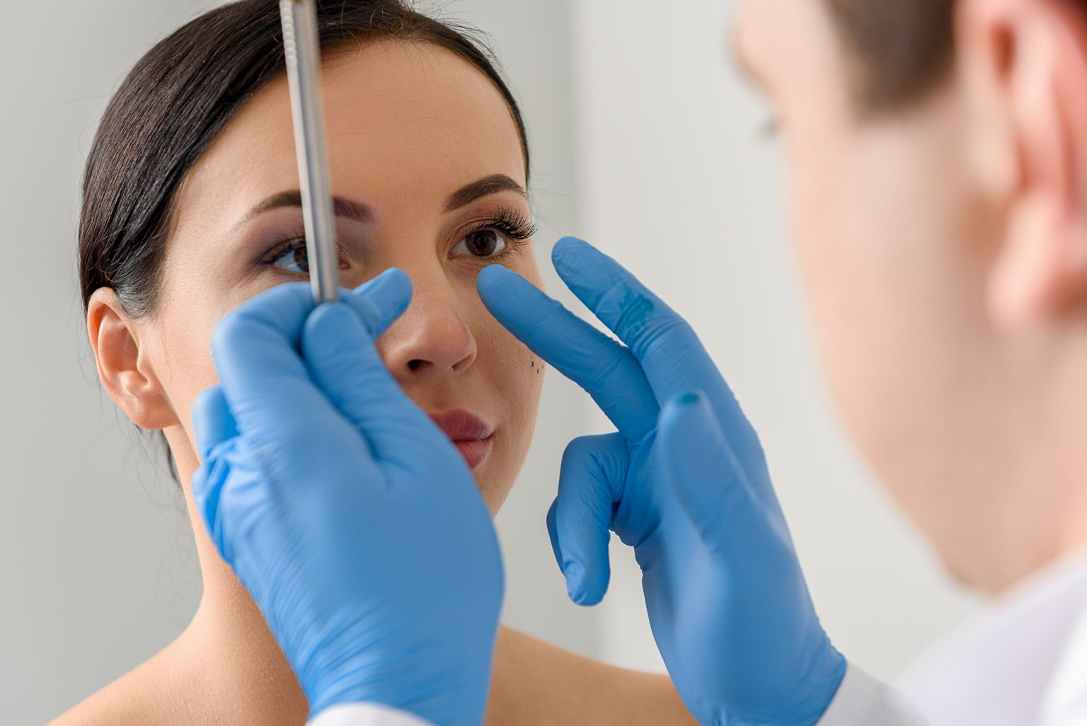 Doctor inspecting the nose of a patient before she undergoes Rhinoplasty also known as a nose job